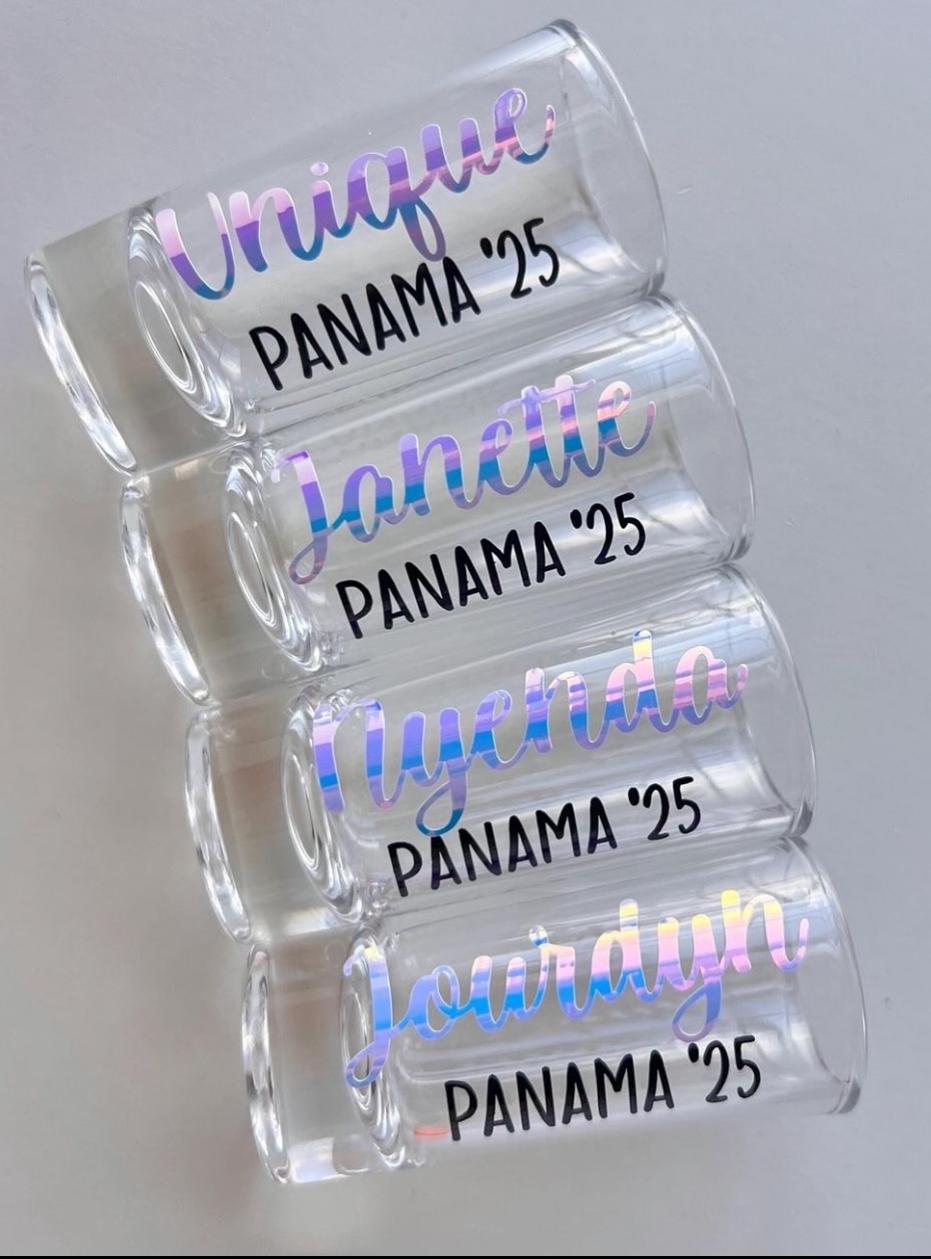 Four custom personalized shot glasses with holographic iridescent name vinyl, laid out on a neutral surface